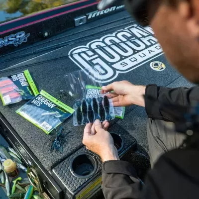 Homem segurando iscas de pesca em embalagem, no barco com logótipo 'GOOGAN SQUAD'.