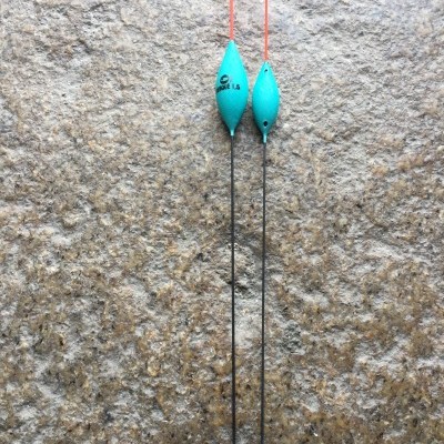 Duas boias de pesca azuis com hastes pretas e antenas vermelhas sobre fundo de pedra cinza.