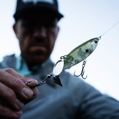 Isca de pesca translúcida com ganchos metálicos segurada por mão masculina