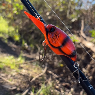 Isca de pesca artificial vermelha e preta com anzóis pendurada numa cana de pesca preta em área exterior