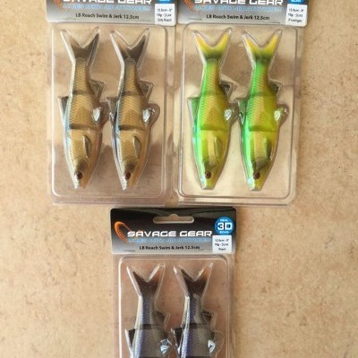 Iscos artificiais Savage Gear em embalagens plásticas, três pares, vários padrões de cores, sobre superfície bege.