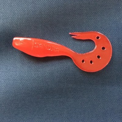 Isca artificial vermelha curva com furos sobre tecido azul escuro