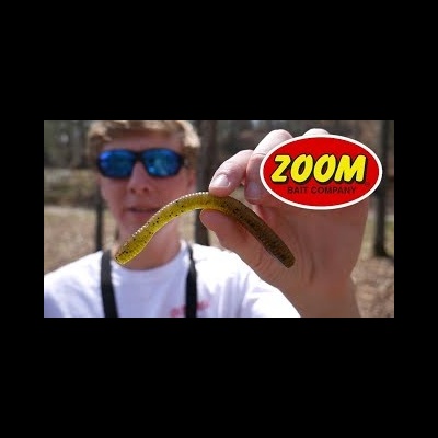 Pessoa segurando isco de pesca verde com pontinhos pretos e logotipo ZOOM BAIT COMPANY