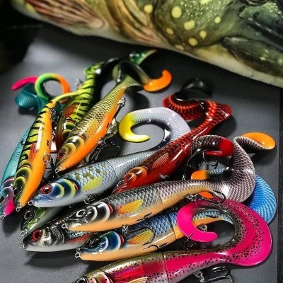 Iscos artificiais coloridos para pesca com vários peixes realistas e ganchos, com peixe verde ao fundo.