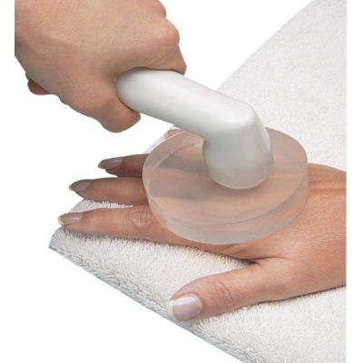 Dispositivo de massagem branco com base redonda translúcida sobre uma mão apoiada em toalha branca.