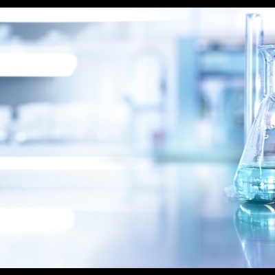 Frascos de laboratório com líquidos coloridos e mãos com luvas azuis manipulando tubos de ensaio