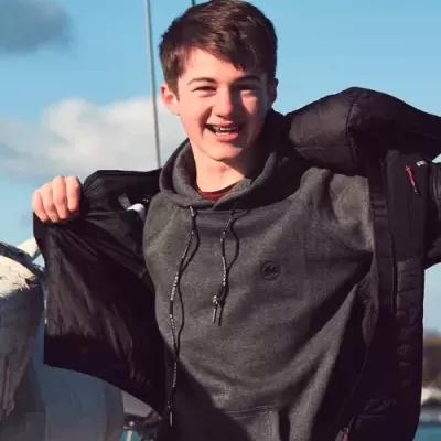 Adolescente com hoodie cinza e casaco preto aberto ao ar livre com céu azul ao fundo