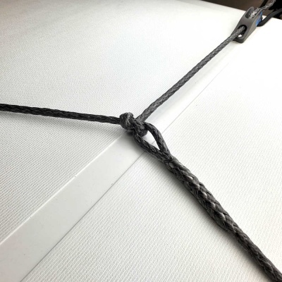 Corda preta com nó e argola metálica sobre fundo branco texturizado