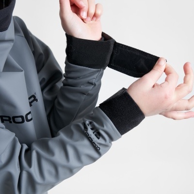 Casaco cinzento com punhos pretos ajustáveis em velcro sendo ajustados por uma mão