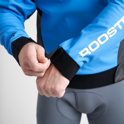 Pessoa a ajustar o punho de uma camisola azul com texto branco ROOSTER e calças cinzentas