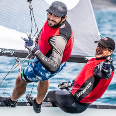 Dois homens a velejar com coletes salva-vidas vermelhos e pretos e roupas desportivas