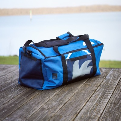 Mala de desporto azul com alças pretas numa superfície de madeira em frente a um lago