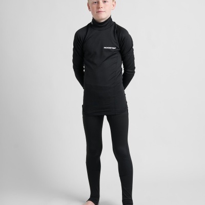 Menino vestido com roupa térmica preta, camisola de gola alta e calças legging, texto branco no peito, de pé descalço