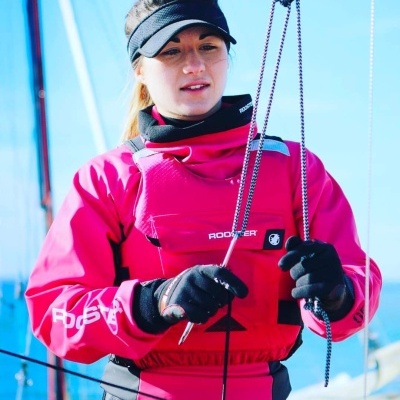 Pessoa com roupa impermeável rosa e luvas pretas em barco com mar ao fundo