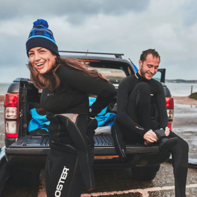 Duas pessoas de fatos de mergulho pretos junto a uma pick-up preta em ambiente exterior, uma usa gorro azul com texto ROOSTER.