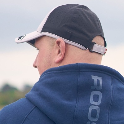 Boné desportivo preto e branco com fecho ajustável usado por homem com camisola azul com capuz 'ROOS'.