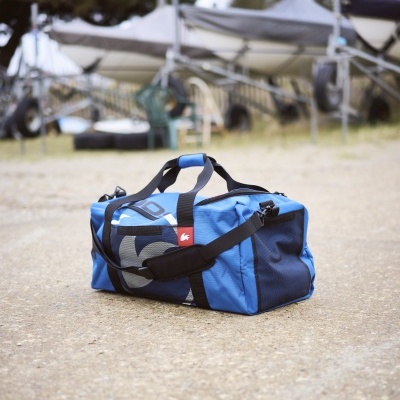 Mala desportiva azul com alças pretas e detalhes cinzentos sobre chão de terra batida