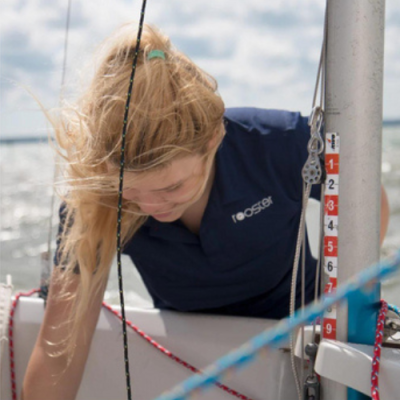 Mulher com colete azul-escuro 'rooster' num veleiro com cabos e mastro numerado