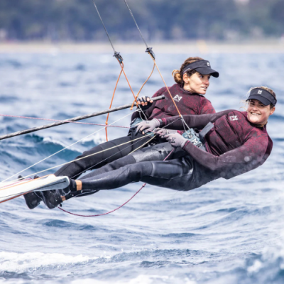 Dois homens praticam vela num veleiro com fatos de neopreno e arnês