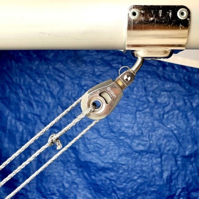 Bloco de vela náutico de metal montado num tubo branco com cordas e fundo azul