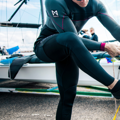 Pessoa com fato de neoprene preto com costuras cor de rosa junto a embarcação branca