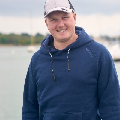 Homem com hoodie azul e boné branco e preto ao ar livre junto à água