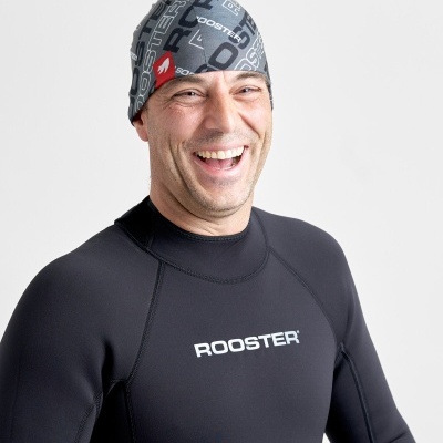Homem a sorrir com fato de mergulho preto e touca cinzenta com texto ROOSTER