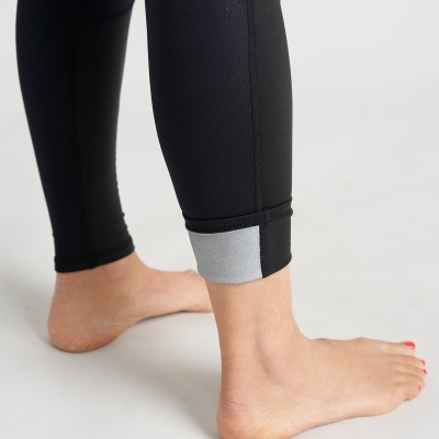 Parte inferior das calças desportivas pretas com detalhes cinza na bainha e pés descalços.