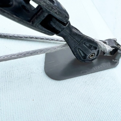 Equipamento náutico com cordas trançadas e peça plástica preta numa superfície cinza.