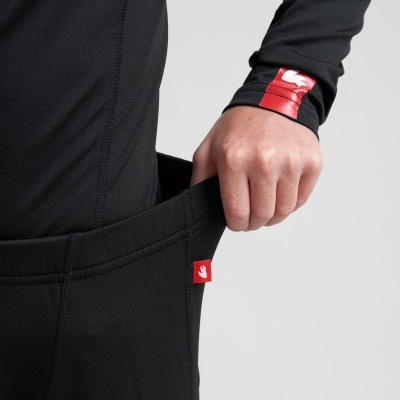 Pessoa com roupa preta puxando o tecido largo da cintura, manga preta com padrão vermelho e branco.