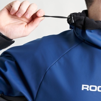 Casaco impermeável azul com capuz e detalhe preto, com a palavra ROCA no peito