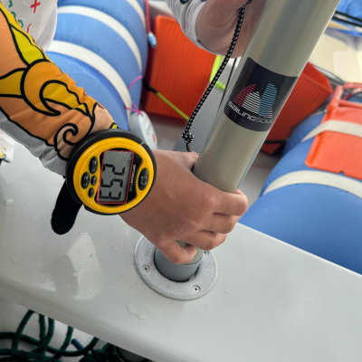 Mão com dispositivo digital segurando barra metálica prateada com etiqueta SAILINGSOUL num barco.