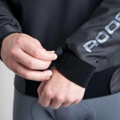 Jaqueta preta com fecho de velcro na manga e calças cinza com remendo acolchoado