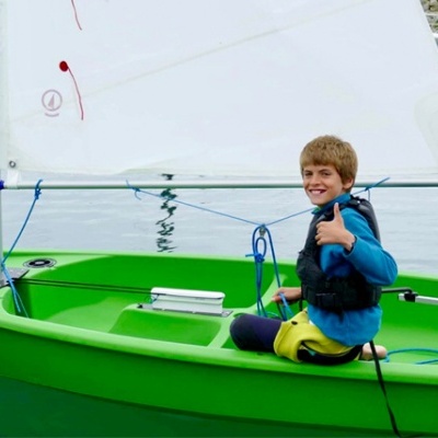 Criança em barco de vela verde com vela branca na água