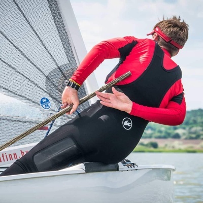 Homem com fato de vela segurando corda num barco à vela branco