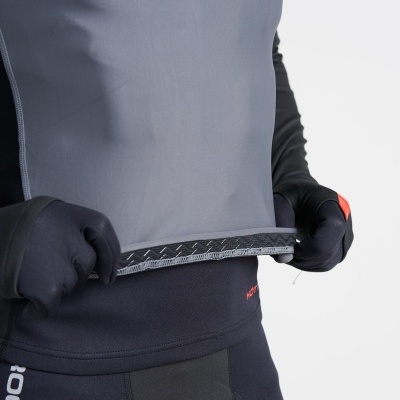 Pessoa vestindo roupa desportiva cinza e preta, segurando a barra da camisa, com luvas pretas e fundo branco.