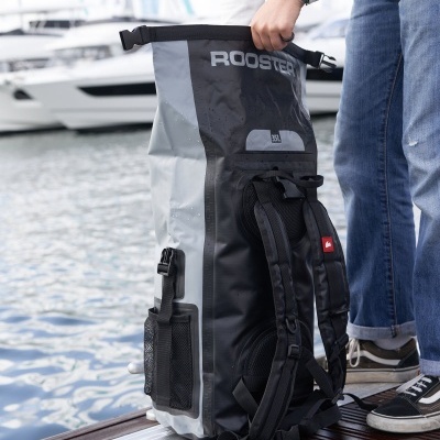 Mochila impermeável preta e cinzenta com texto ROOSTER junto a pessoa num cais