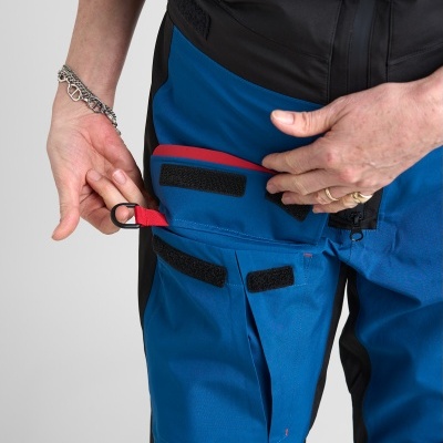 Calças de trabalho azuis com bolsos de velcro e detalhe vermelho, com fita e ilhó metálico