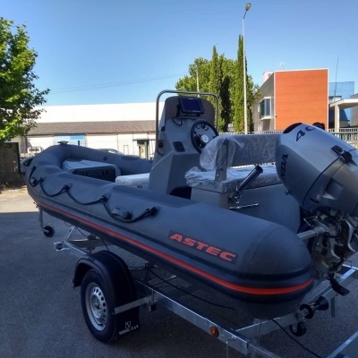 Barco insuflável cinzento com motor de popa num reboque ao ar livre