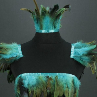 Roupa decorada com penas turquesa e verdes sobre manequim preto