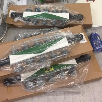 Suportes de parede pretos com ganchos em metal embalados em plástico, sobre caixas de cartão