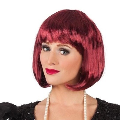 Mulher com peruca vermelha curta e franja, vestido preto e colar de pérolas