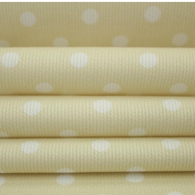 Tecido amarelo claro com bolinhas brancas empilhado e fundo bege com bolinhas brancas maiores