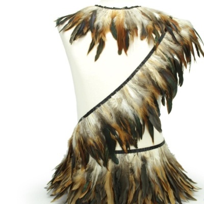 Traje decorativo com penas castanhas, pretas e bege em manequim branco