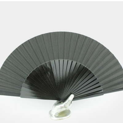Leque preto com lâminas de madeira e pano, exibido numa base de vidro.