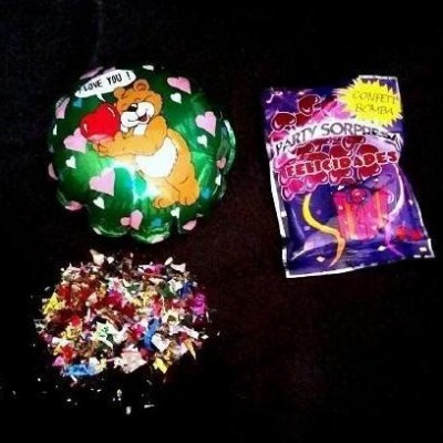 Balão verde com urso e coração, saco de confetti coloridos e confetti espalhados no fundo preto