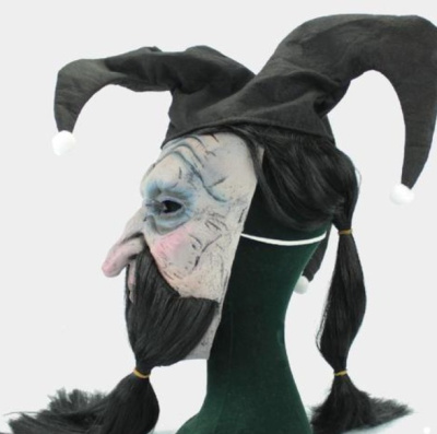 Máscara de personagem com pele enrugada, chapéu preto com bolas brancas e cabelo em tranças pretas