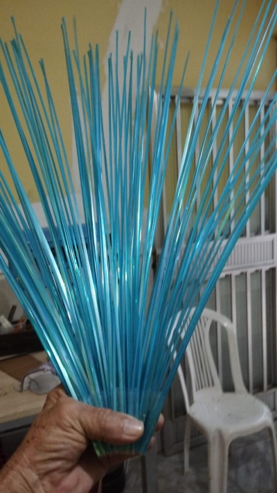 Mão segurando varas finas azuis translucidas em ambiente doméstico