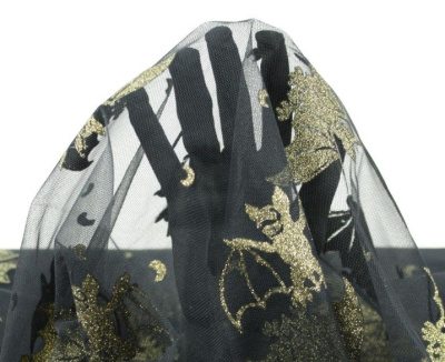 Tecido preto transparente com padrão dourado de morcegos e outros motivos, com mão por baixo do tecido