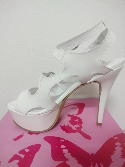 Sandália branca de salto alto com plataforma e design recortado sobre caixa rosa com borboletas vermelhas